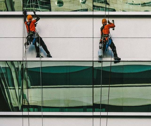 Two men suspended down the side of a building cleaning the cladding between floors on an office building in the West Midlands.