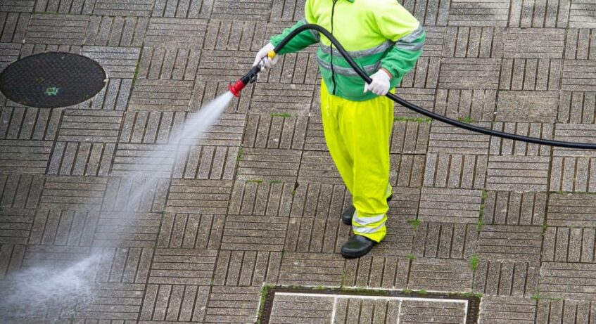 man in safety suit power washing floor